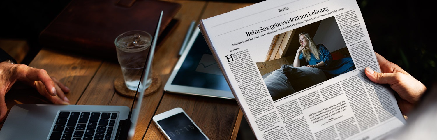 Zeitung in der Hand vor Schreibtisch